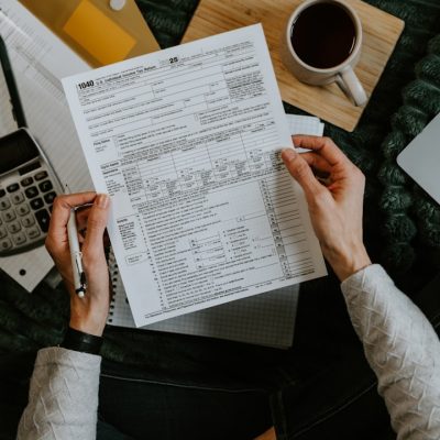 Hands holding tax forms with calculator and laptop.