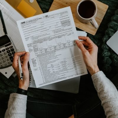 Hands holding tax forms with calculator and laptop.